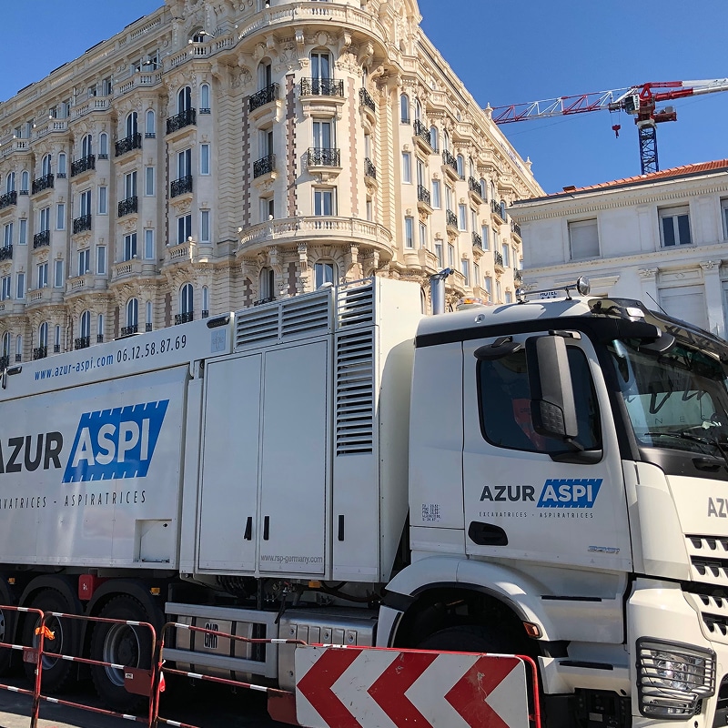 Camion AZUR ASPI (Excavatrices - Aspiratrices) devant un grand bâtiment historique orné. Contacts: azur-aspi.com et 06.12.58.87.69.