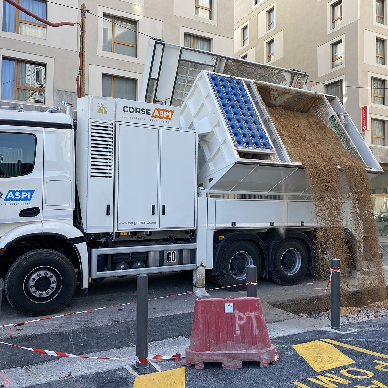 Camion aspiratrice CORSE ASPI (www.rsp-germany.com) décharge des gravats sur un chantier urbain. La benne révèle des filtres bleus.