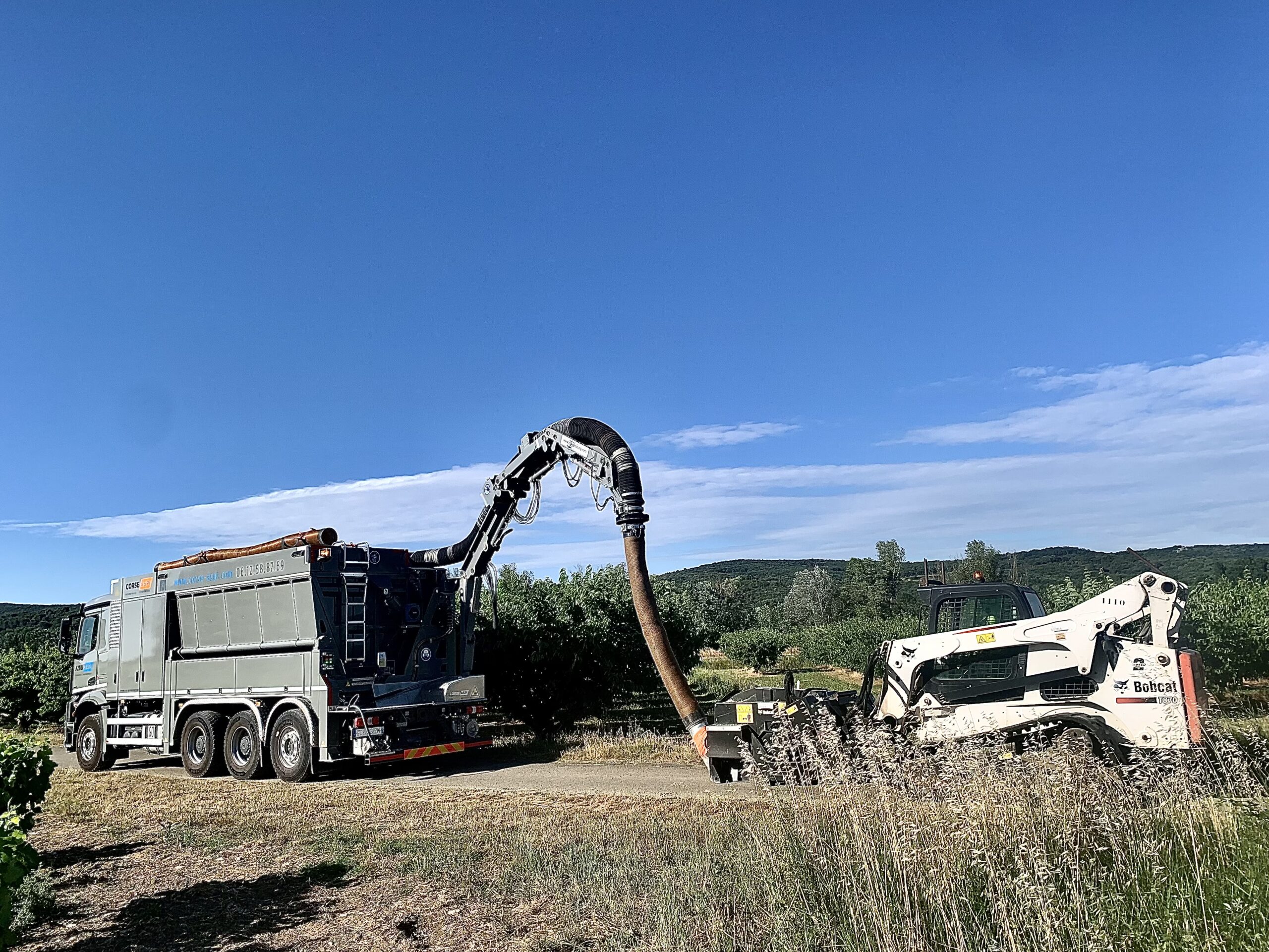 Camion aspirateur Corse Aspi relié à un Bobcat T870 pour du terrassement par aspiration en extérieur.