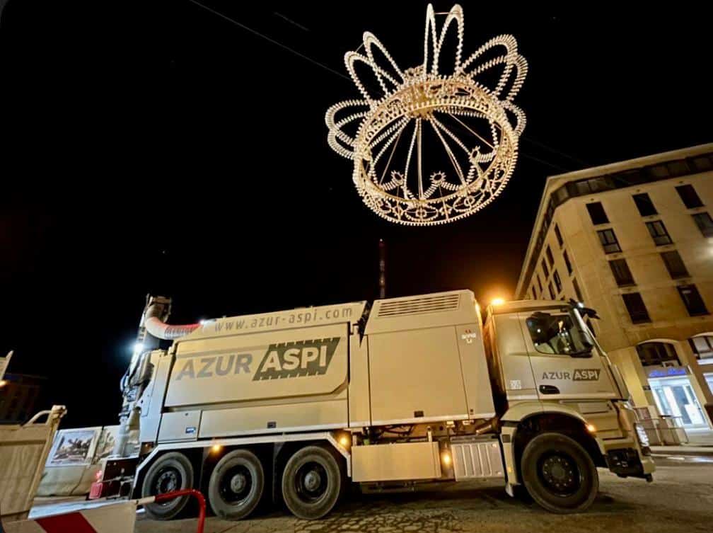 Camion aspiratrice Azur Aspi sous les lumières de Noël Camion aspiratrice Azur Aspi stationné sous une couronne lumineuse géante dans une rue la nuit.