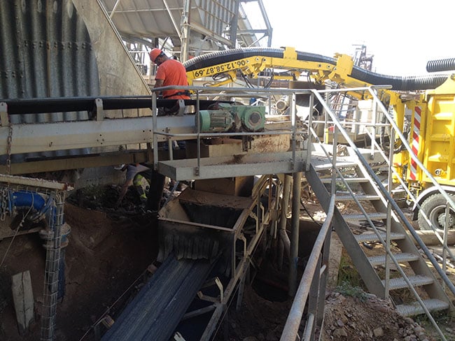 Maintenance de convoyeur : camion aspirateur sur chantier. Ouvrier en orange effectue la maintenance d'un convoyeur sur une plateforme industrielle. Un camion aspirateur jaune est visible à droite. Tél : 06.12.58.87.69.