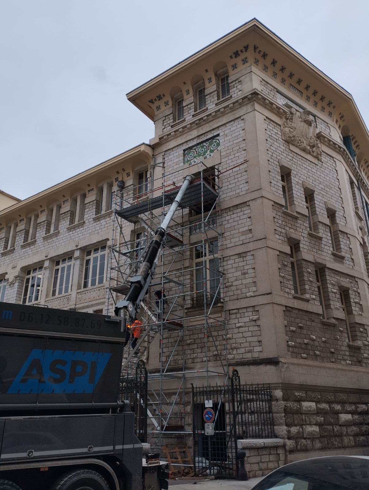Camion ASPI utilisant un tuyau d'aspiration sur l'échafaudage d'un bâtiment historique en pierre en rénovation.