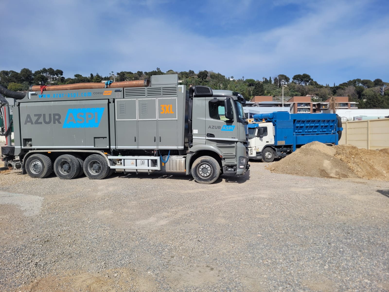 Camion aspiratrice excavatrice Azur Aspi 3XL gris sur un chantier avec un tas de terre sous un ciel bleu.