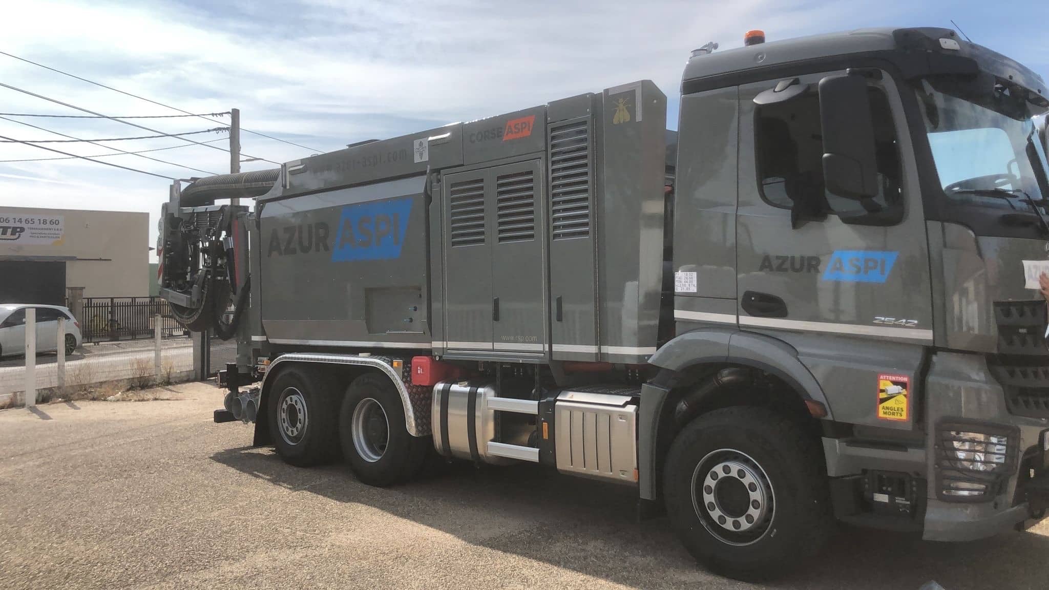 Camion aspirateur gris Azur Aspi pour terrassement, avec bras d'aspiration articulé sur un chantier extérieur.