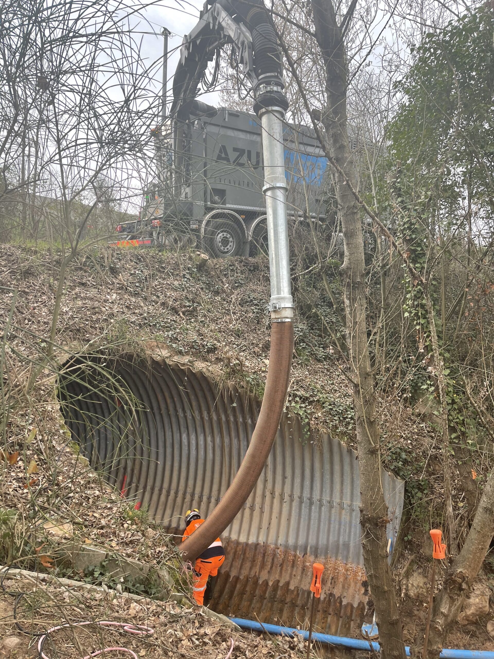Aspiratrice excavatrice AZURA opérant dans un tunnel métallique avec un ouvrier en équipement de protection orange.