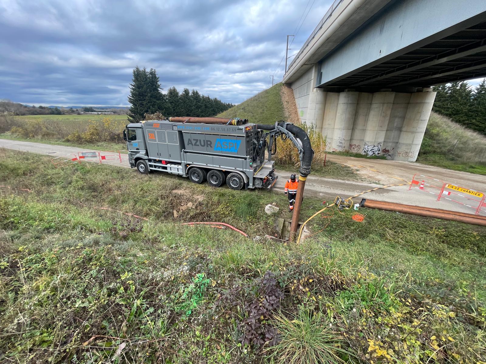 Camion aspirateur AZUR ASPI opérant sous un pont pour des travaux de terrassement par aspiration.