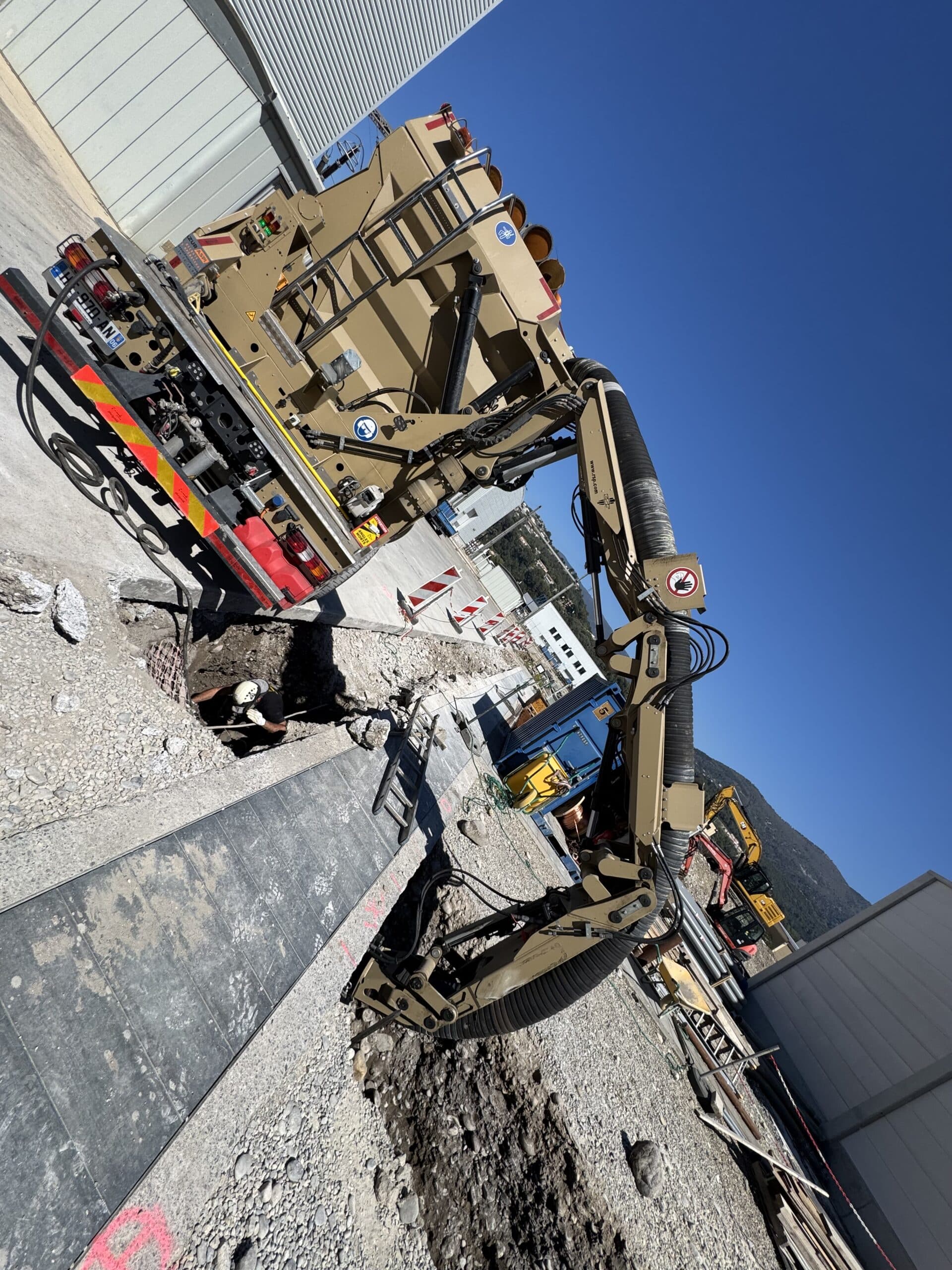 Camion aspirateur RSP excavant une tranchée sur un chantier, bras articulé en action et ouvrier au travail.