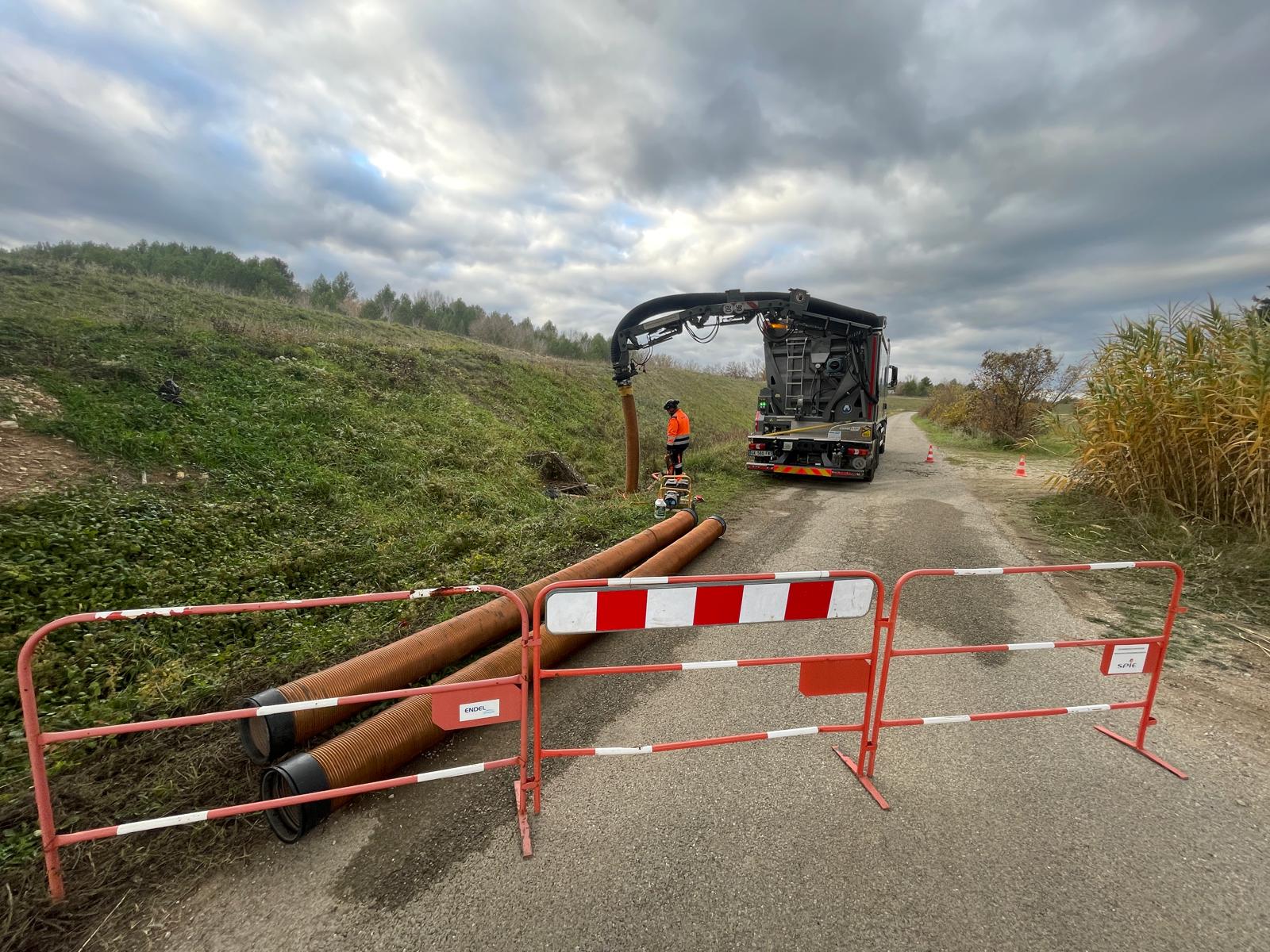 Technicien et camion hydrocureur en intervention d'assainissement avec barrières Endel, Spie et tuyaux orange.