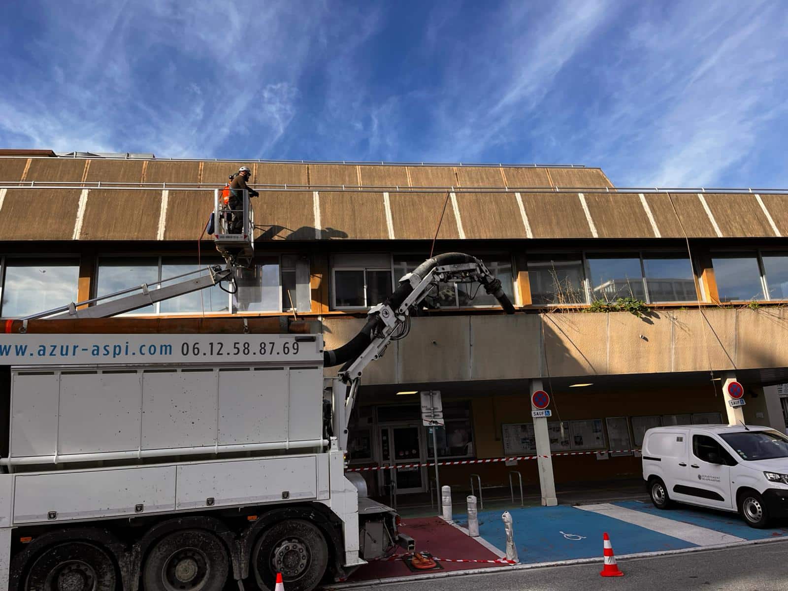 Camion suceuse Azur Aspi (06.12.58.87.69) et ouvrier en nacelle intervenant sur la façade d'un immeuble de bureaux.