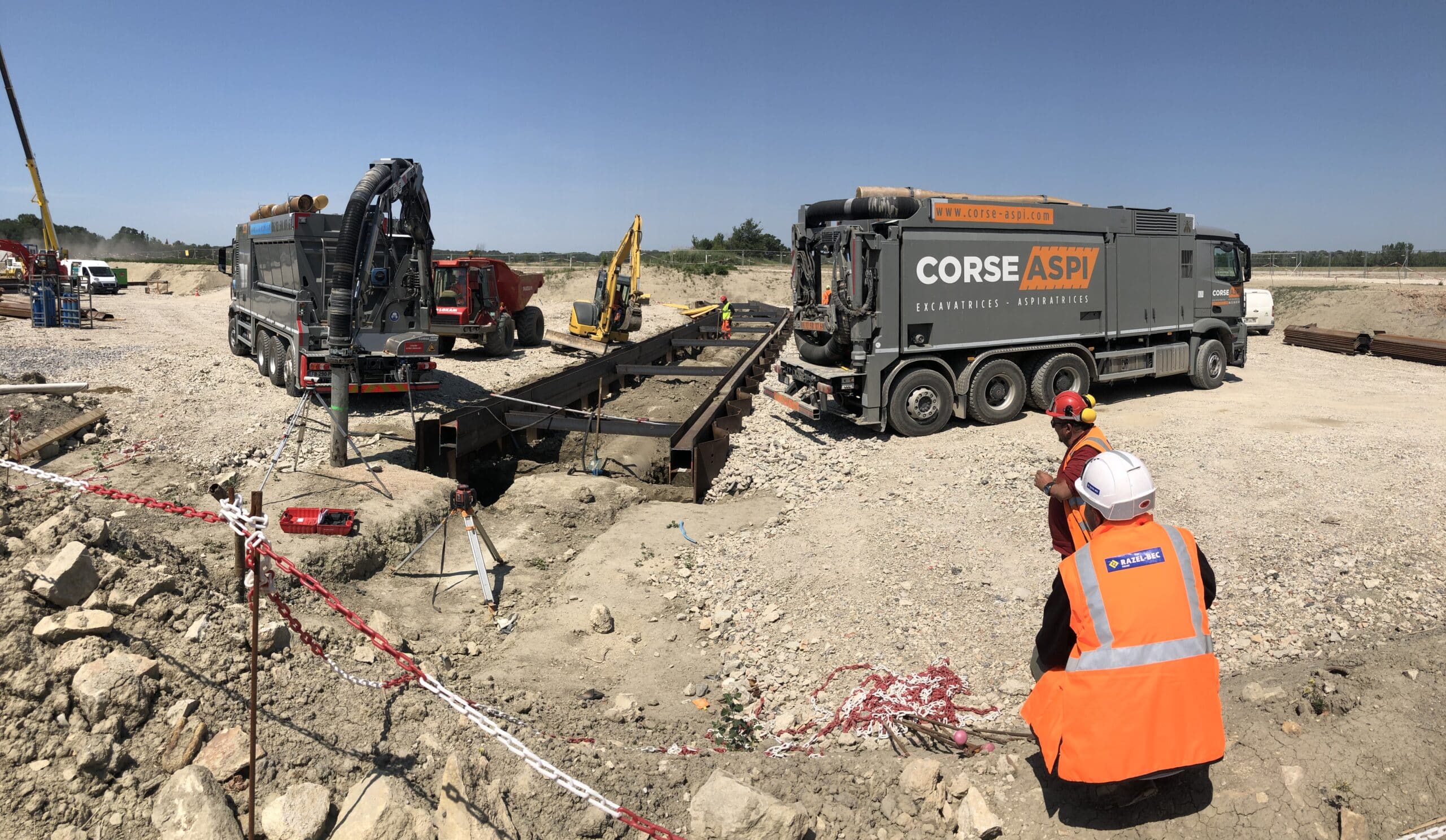 Camions aspirateurs Corse Aspi et ouvriers Razel-Bec sur un chantier de terrassement avec excavatrices.