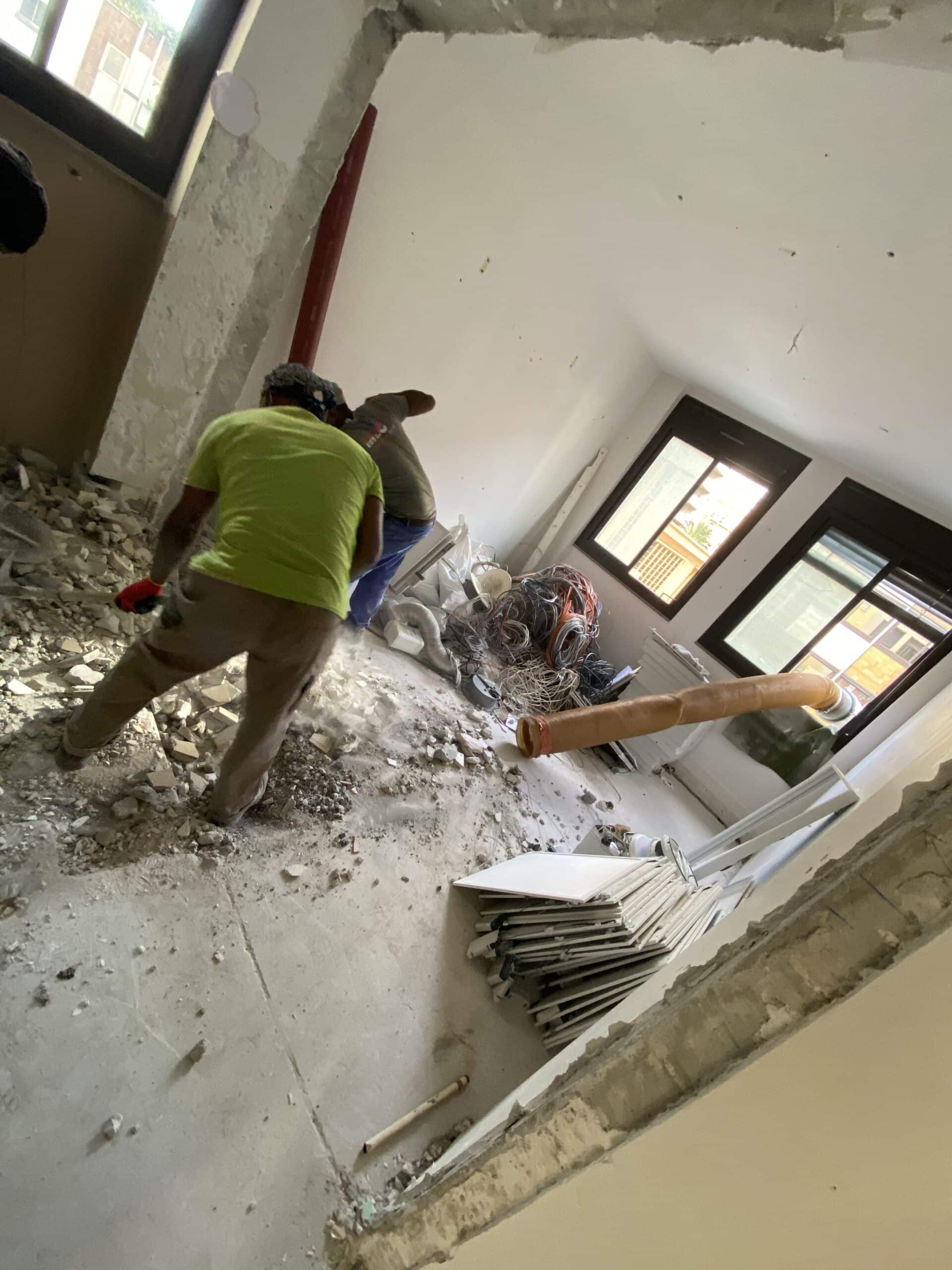 Deux ouvriers en plein travail de démolition intérieure sur un chantier de rénovation avec gravats et câbles au sol.