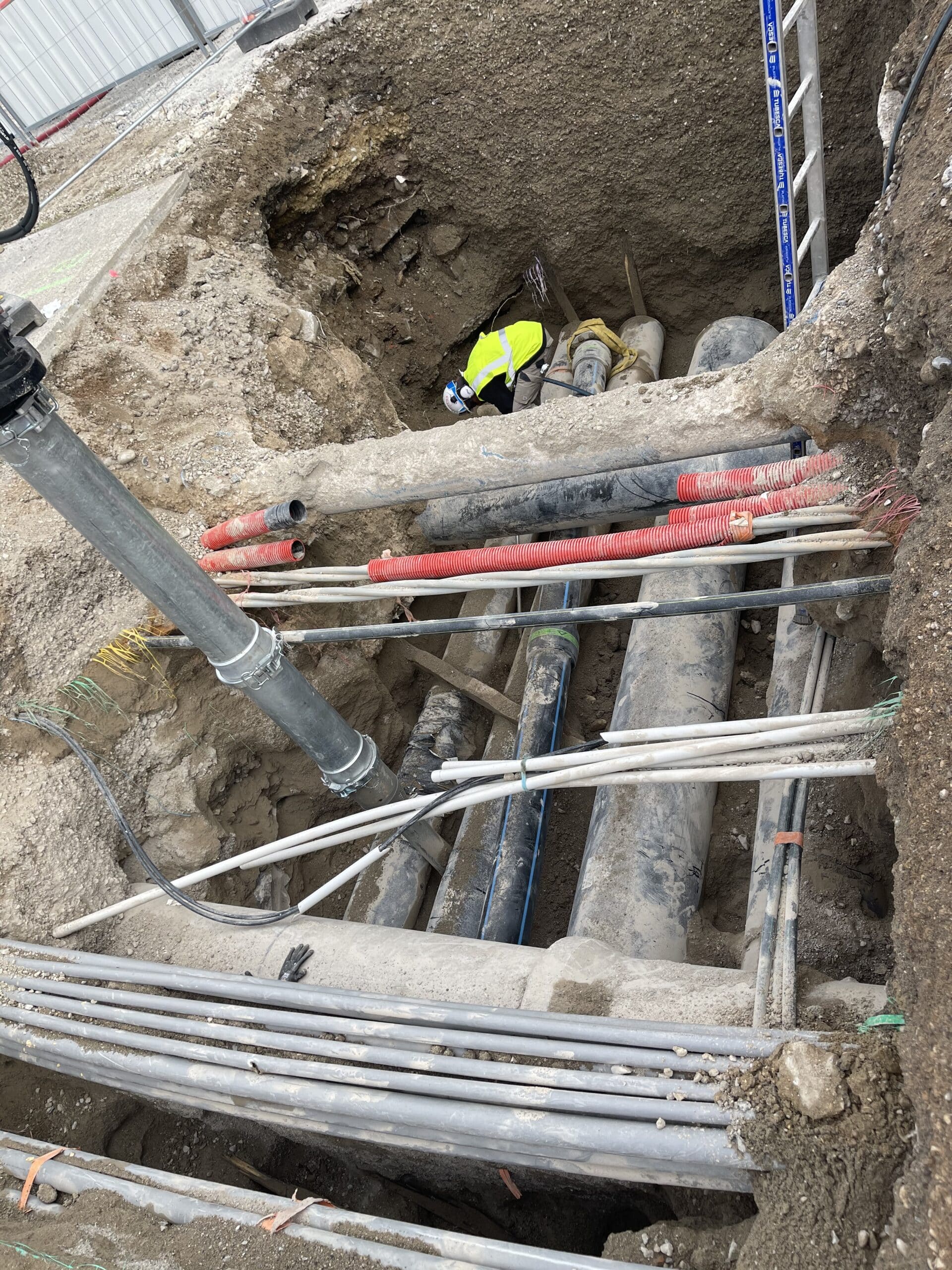 Ouvrier en gilet jaune dans une tranchée de chantier avec canalisations et fourreaux de réseaux souterrains.