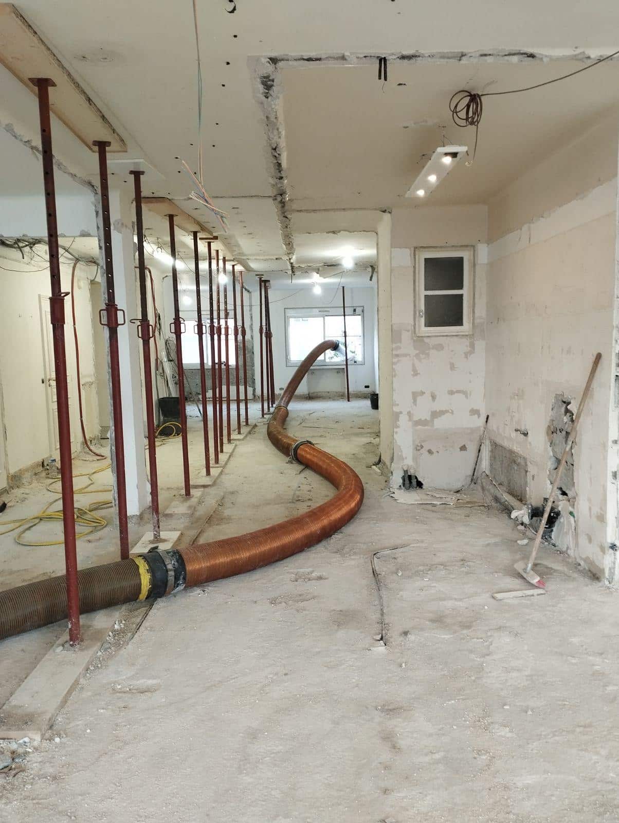 Chantier de rénovation intérieure avec étais de soutien rouges et grand tuyau d'extraction flexible au sol.