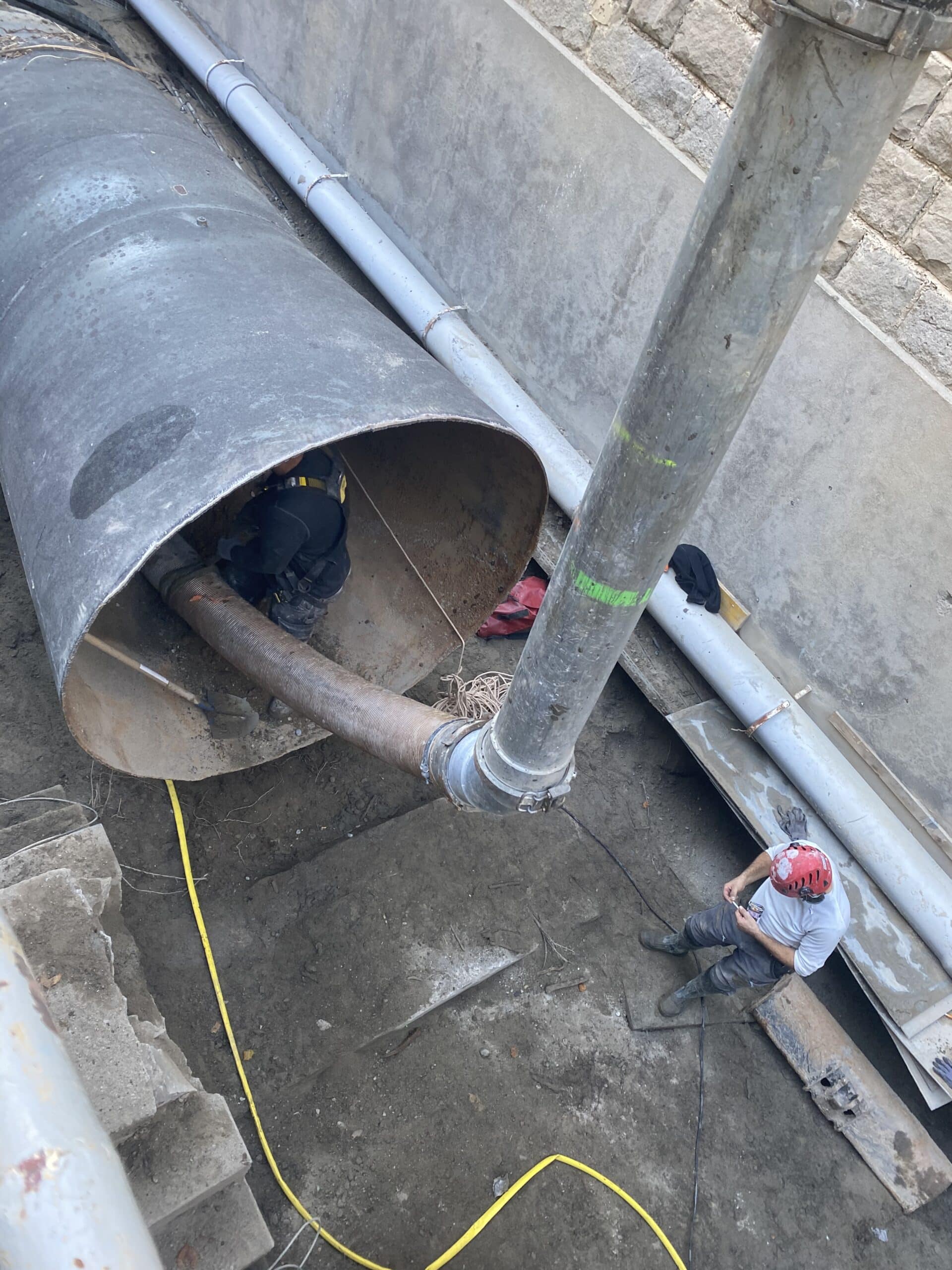 Ouvriers sécurisés travaillant sur une canalisation métallique imposante dans une zone d'excavation.