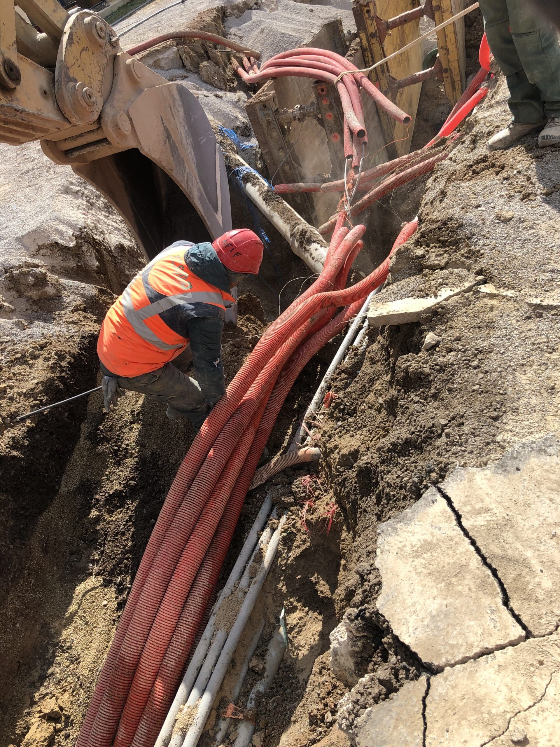 Ouvrier avec casque Hafif installant des gaines électriques rouges dans une tranchée de chantier de travaux publics.