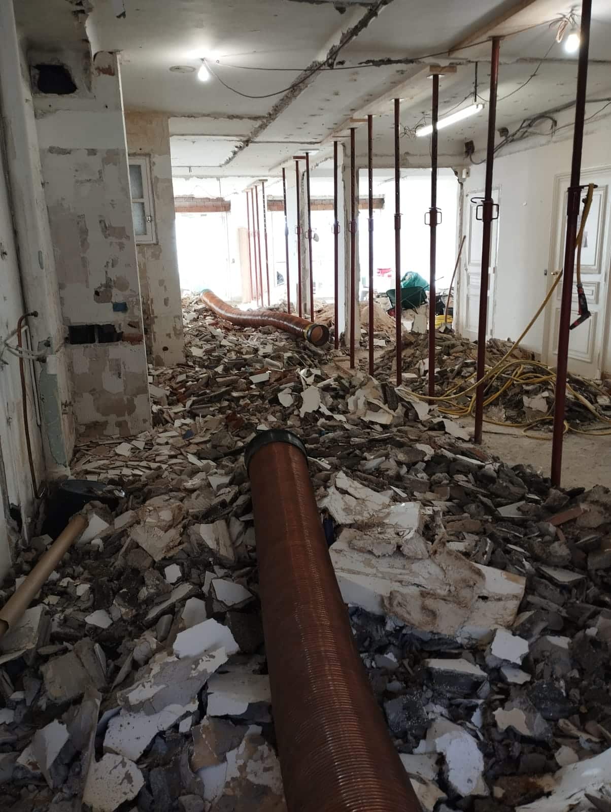 Chantier de démolition intérieure avec gravats, étais de soutien métalliques et tuyaux d'évacuation flexibles.