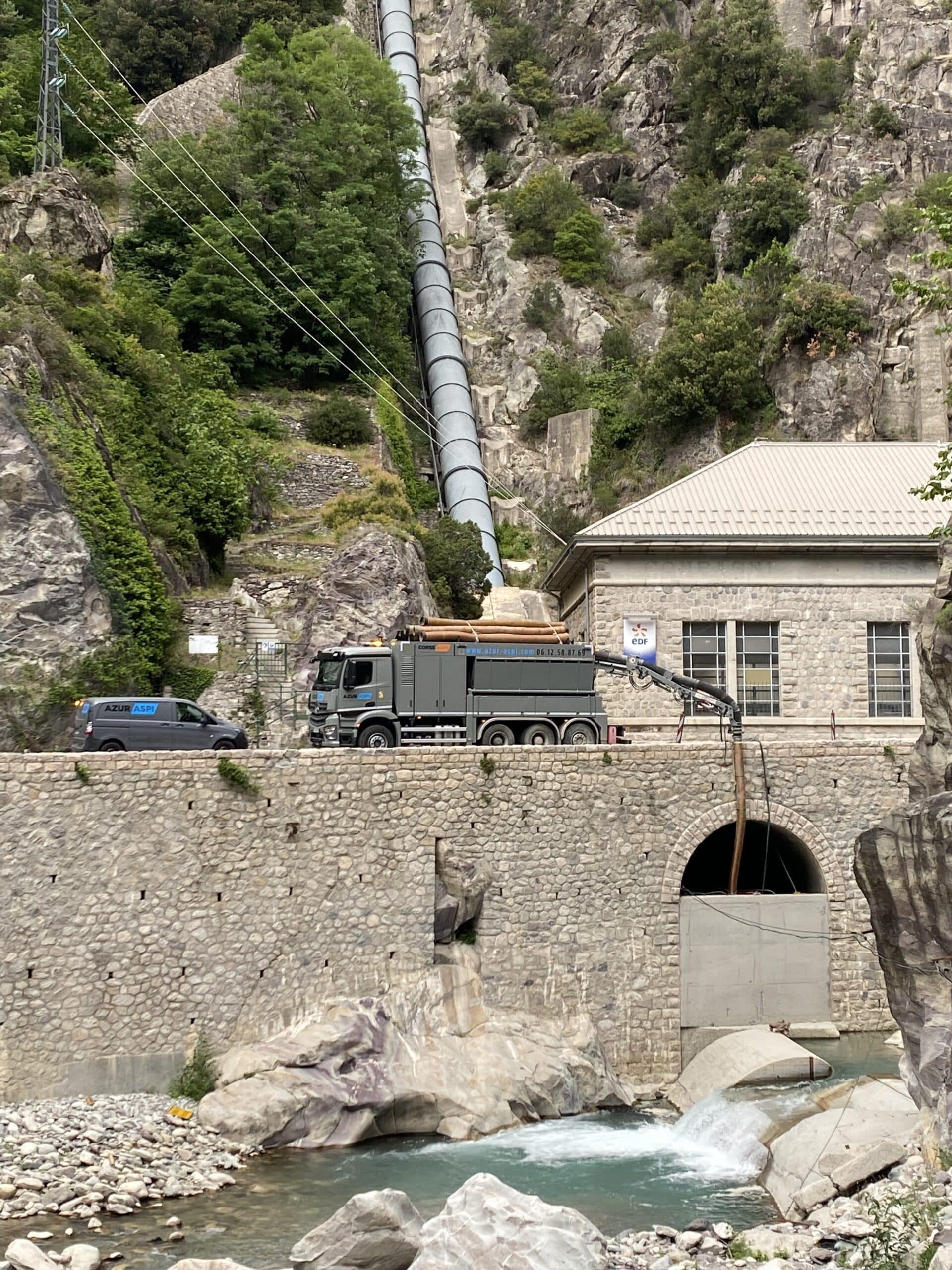 Camion Azur Aspi intervenant sur un site hydroélectrique EDF avec une grande conduite forcée en arrière-plan.