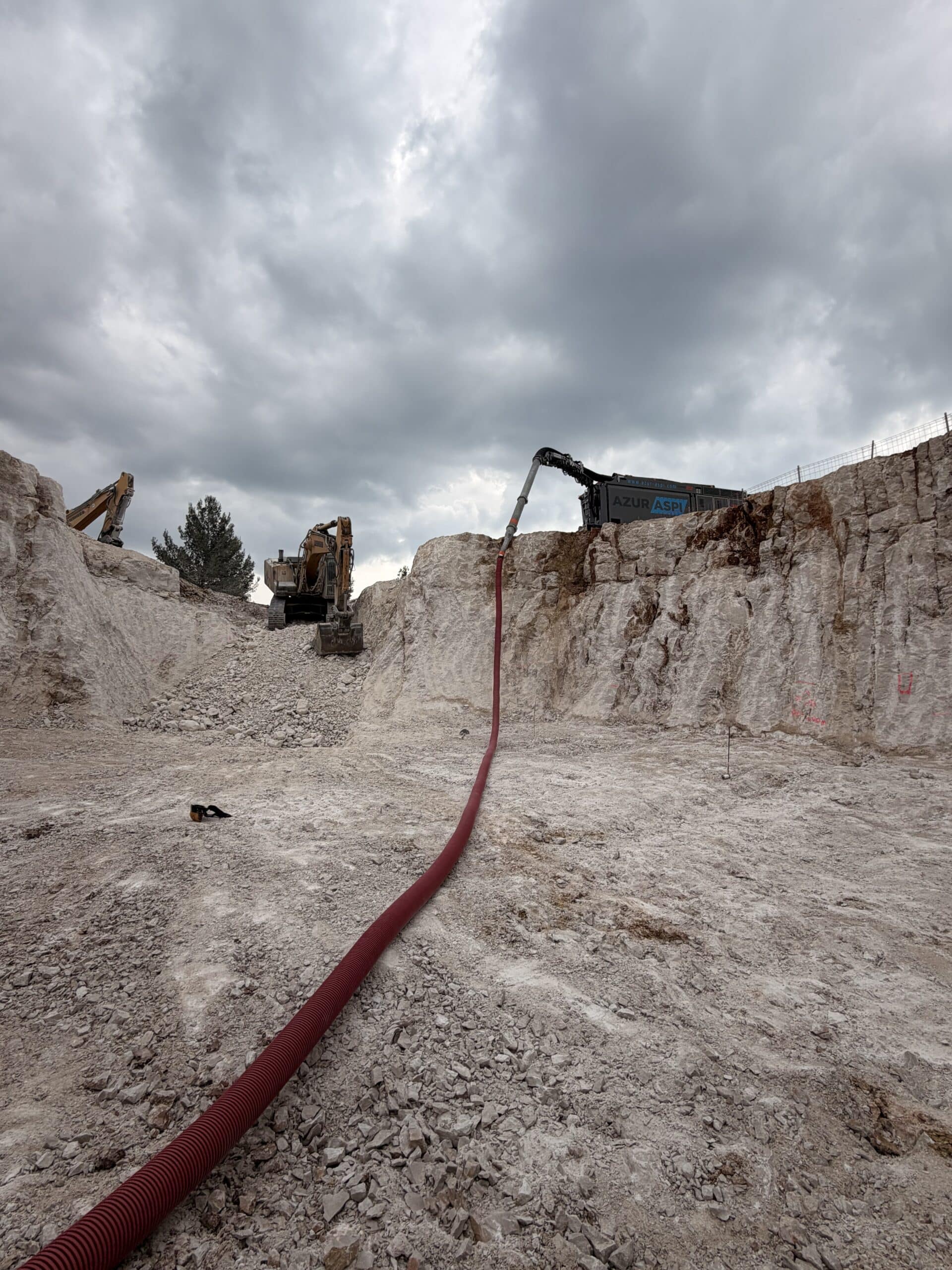 Aspiration de débris Azur Aspi via un long tuyau rouge dans une excavation rocheuse avec pelleteuses.