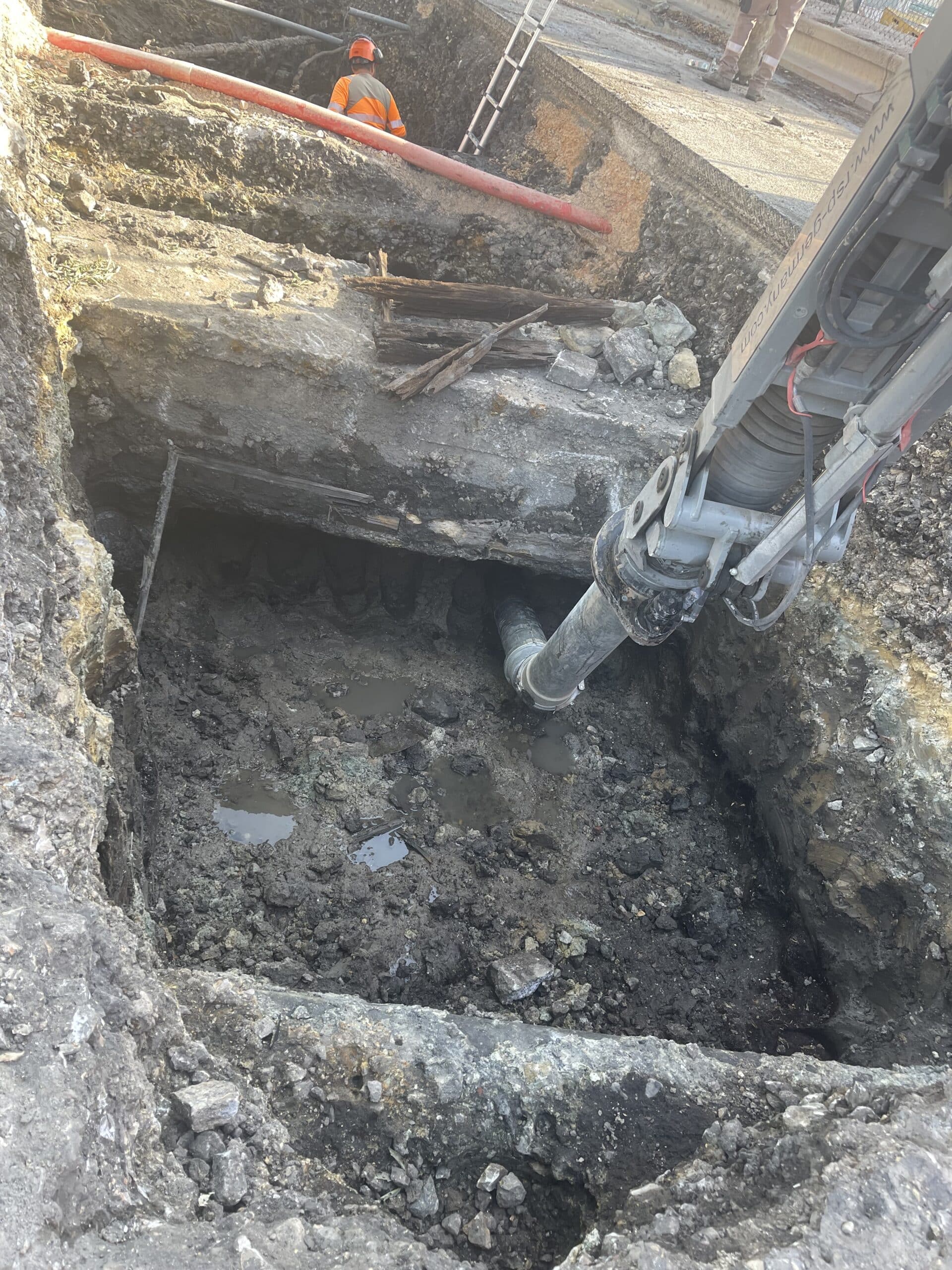 Chantier d'excavation par aspiration avec une buse RSP dans une fosse boueuse près d'un ouvrier en gilet orange.