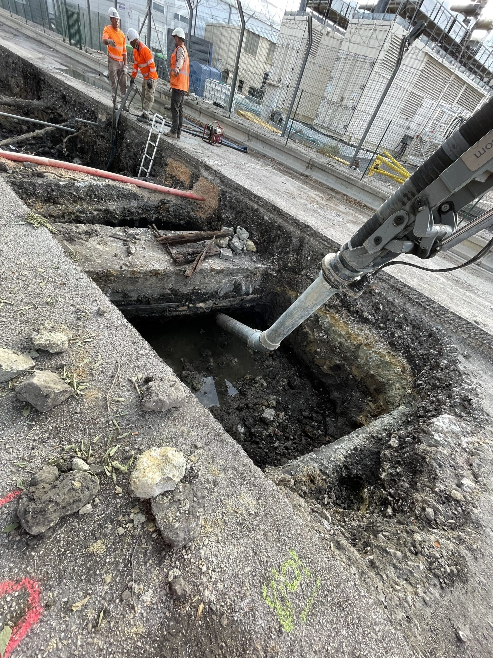 Ouvriers et excavatrice aspiratrice sur un chantier de terrassement urbain avec tranchée profonde dans la chaussée.
