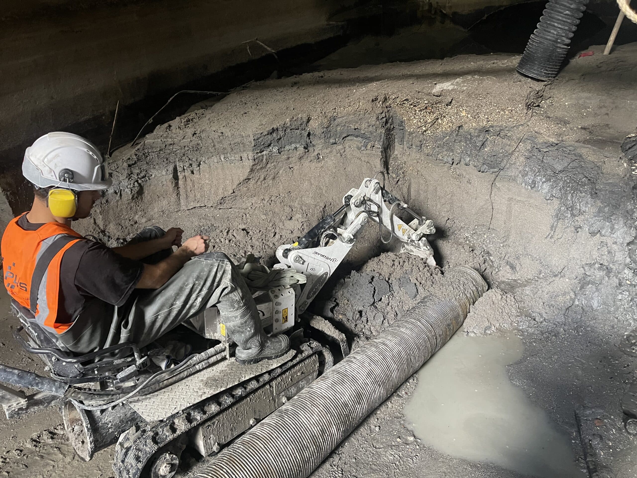 Opérateur pilotant une mini-pelle Gerotto pour une excavation précise dans un tunnel sombre et boueux.