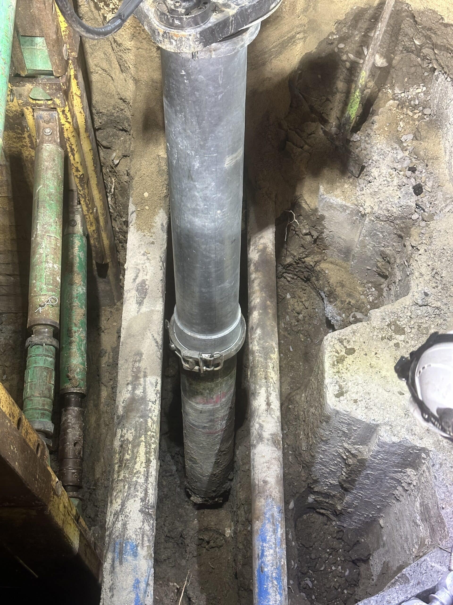 Tuyau métallique vertical dans une excavation avec étaiement hydraulique et poutres de support sur un chantier.