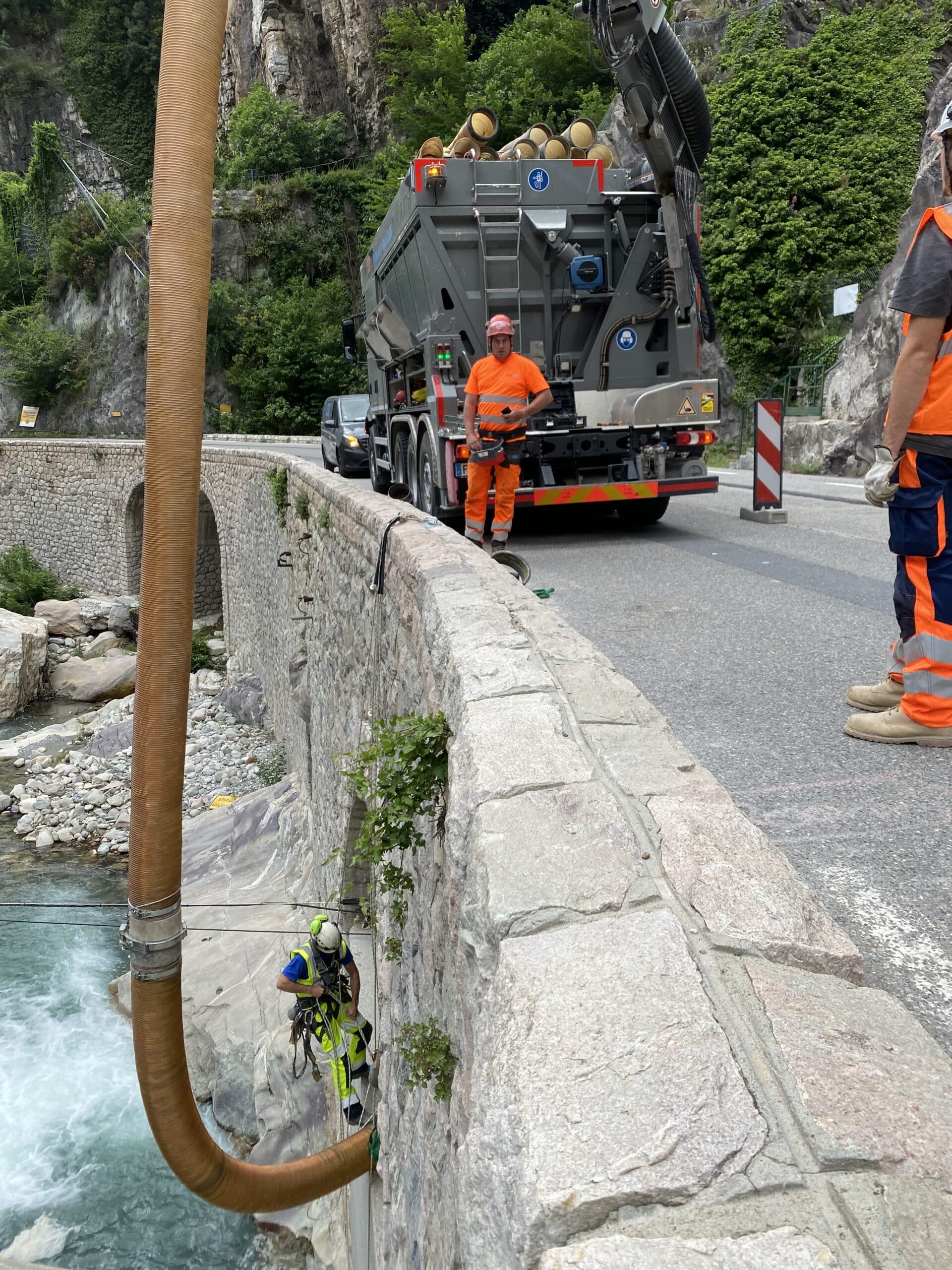 Ouvrier cordiste en rappel et camion aspirateur pour la maintenance d'un pont en pierre au-dessus d'une rivière.