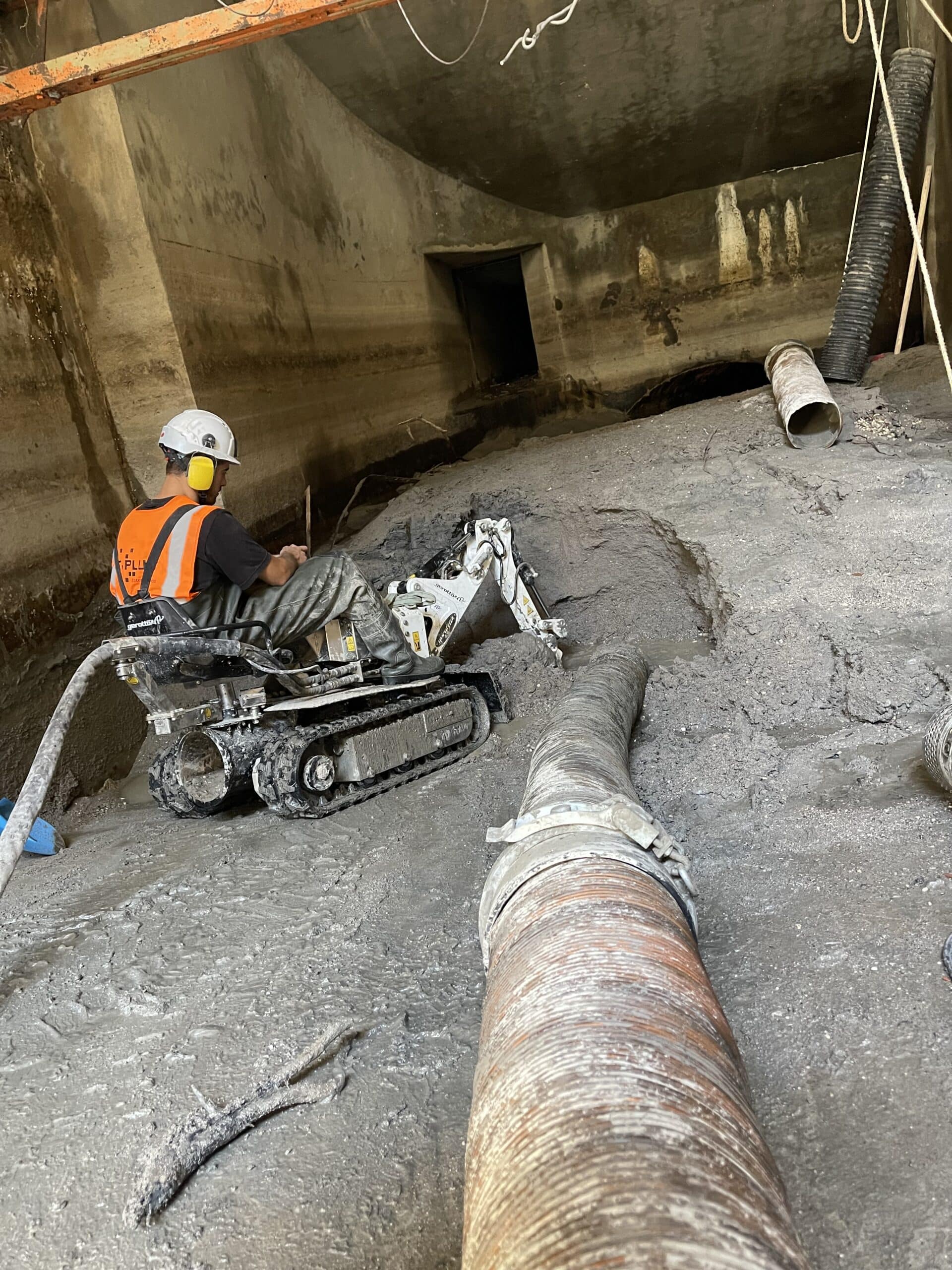 Ouvrier pilotant un robot de curage dans un tunnel d'assainissement boueux avec tuyaux industriels.