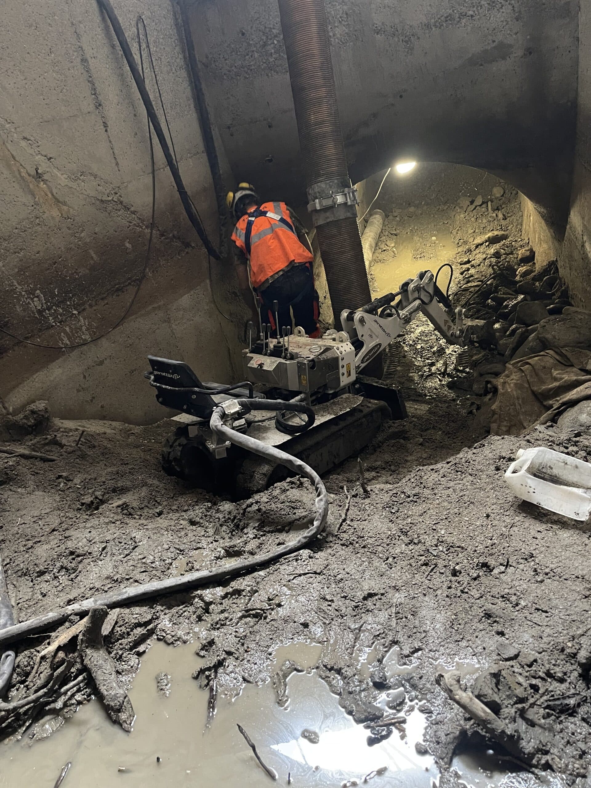 Ouvrier avec robot d'excavation Gerotto et tuyau d'aspiration dans un tunnel étroit et boueux.