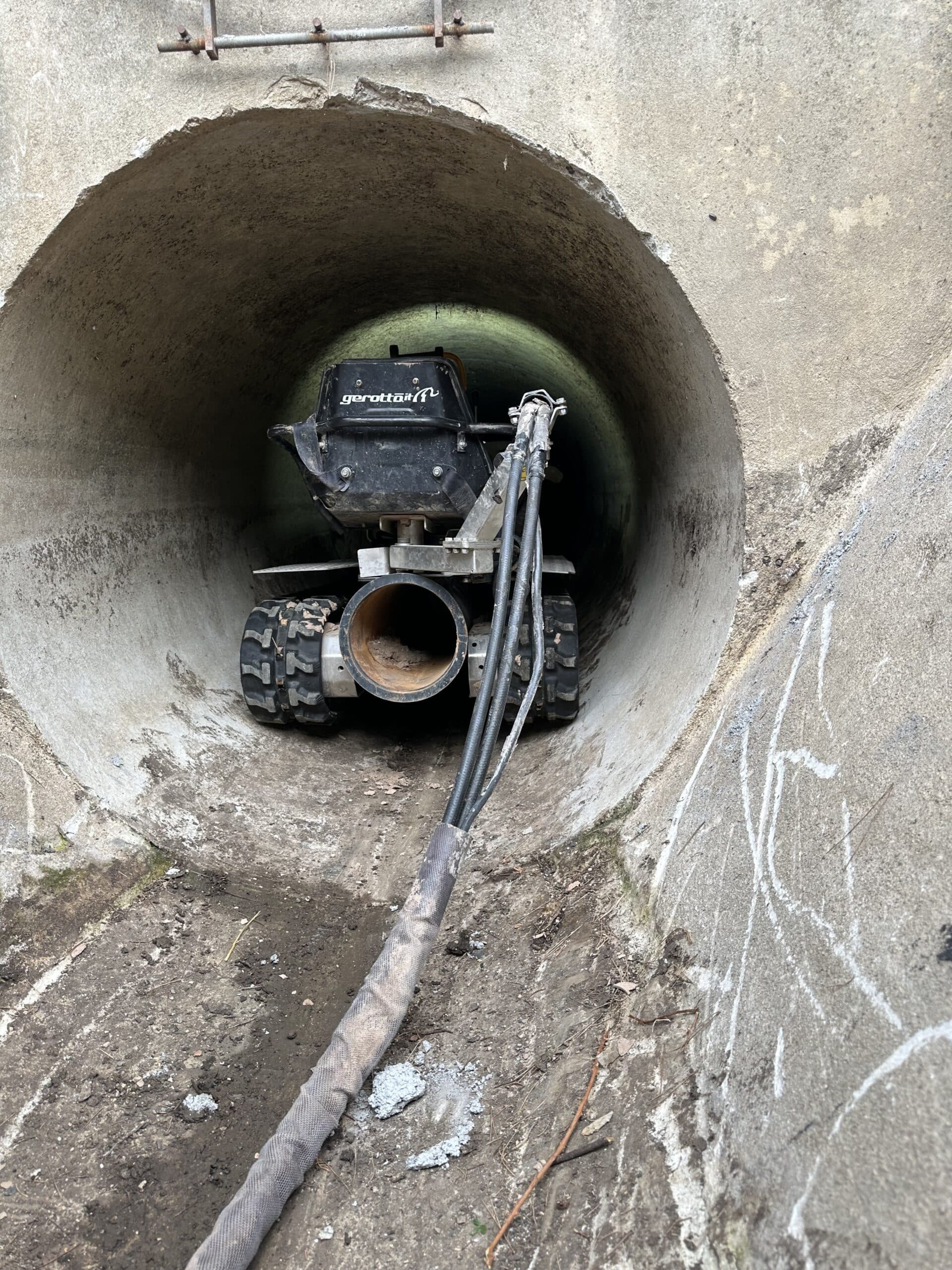Robot Gerotto sur chenilles pour le curage d'une canalisation en béton, avec ses tuyaux de raccordement.