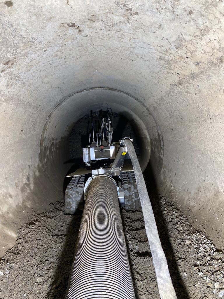 Robot à chenilles installant un tuyau annelé flexible dans un tunnel en béton pour la réhabilitation de canalisations.