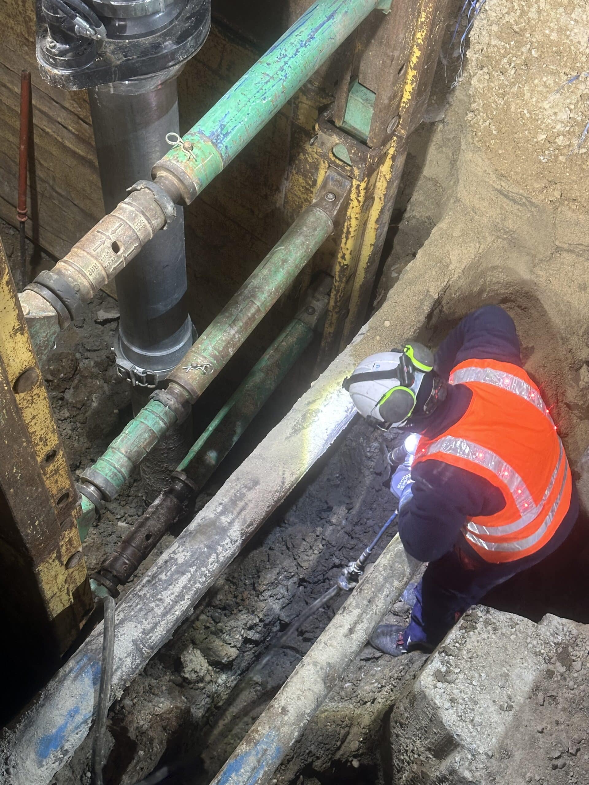 Ouvrier équipé travaillant dans une tranchée blindée lors de travaux de canalisations souterraines.