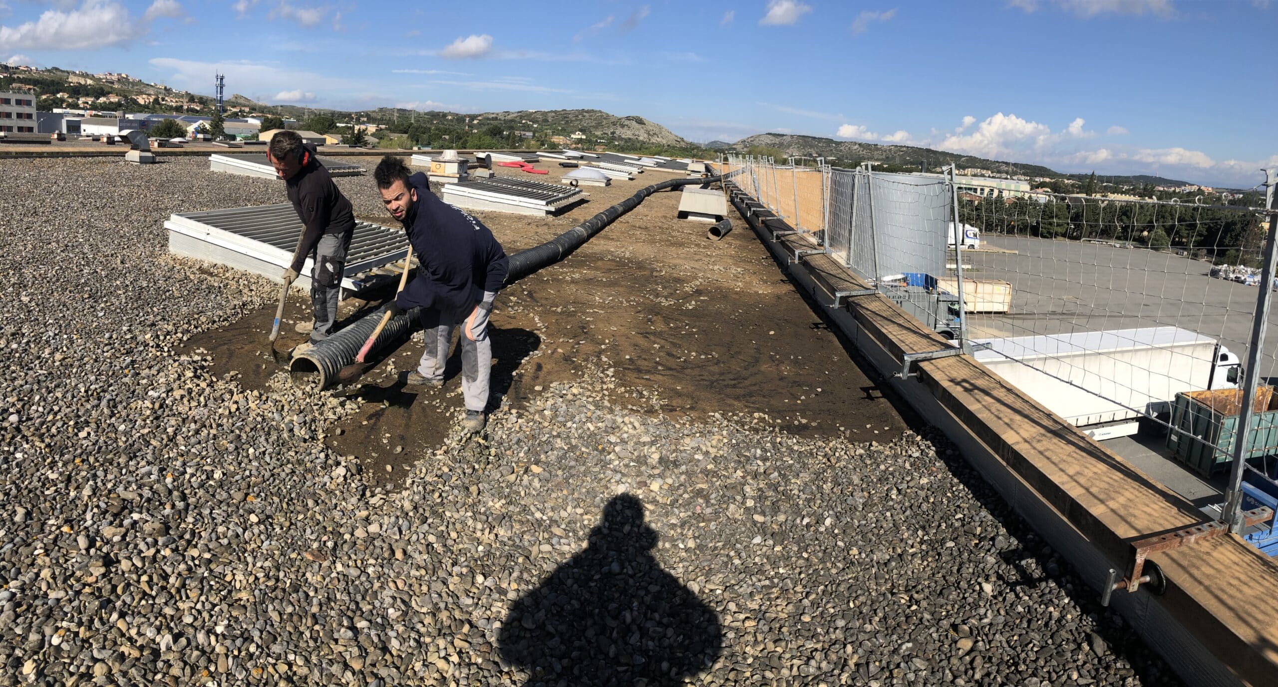 Ouvriers évacuant du gravier avec un tuyau d'aspiration sur une toiture terrasse industrielle sécurisée.