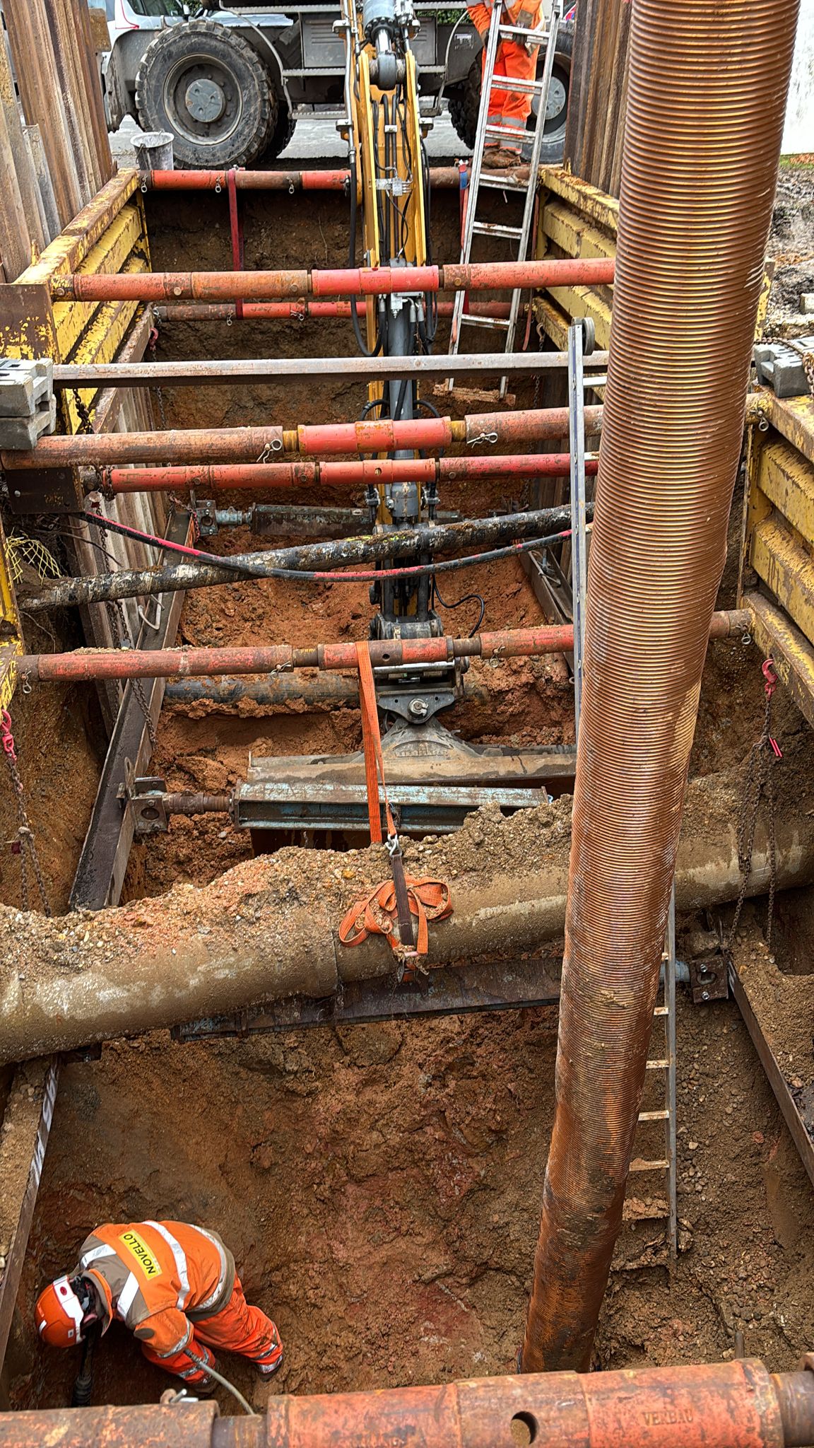 Ouvrier Novello travaillant dans une tranchée sécurisée par blindage métallique et vérins sur un chantier de BTP.