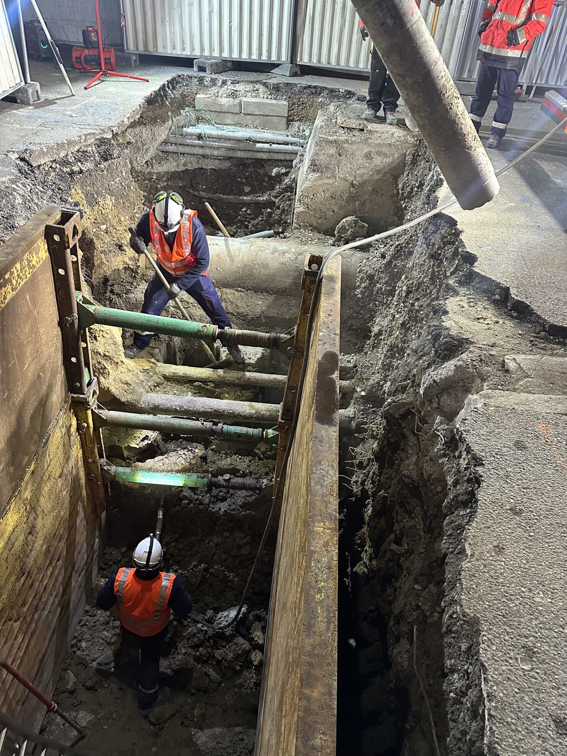 Ouvriers travaillant dans une tranchée sécurisée avec blindage métallique et vérins lors d'un chantier urbain.