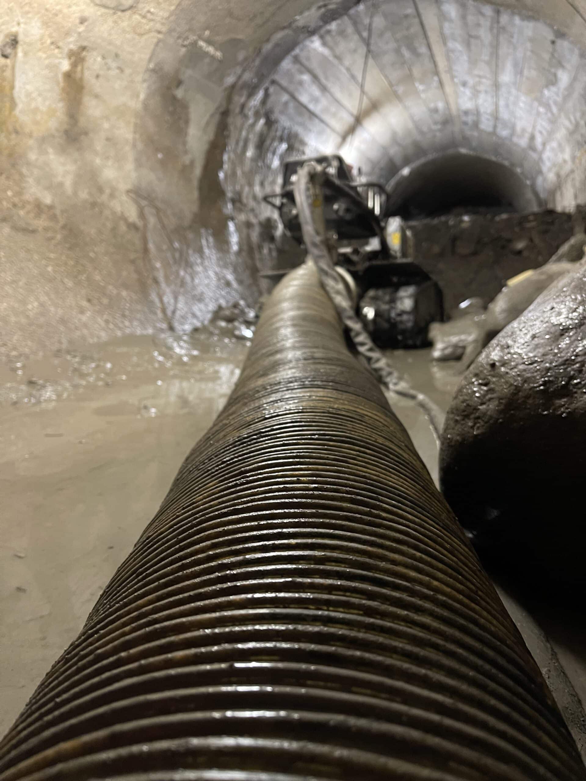 Gros tuyau annelé flexible dans un tunnel en construction humide avec équipement de forage à l'arrière-plan.